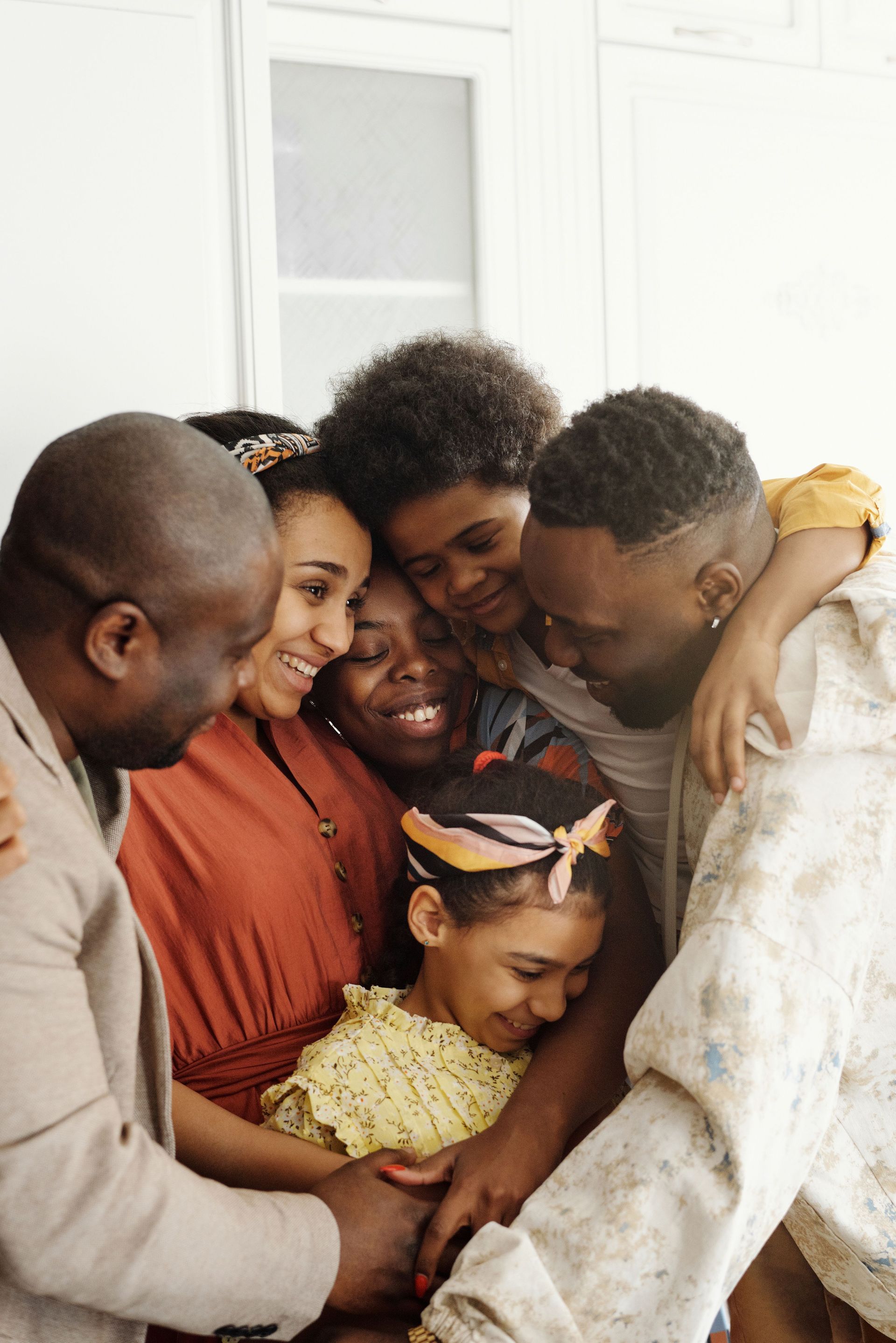 Group of people hugging closely indoors, smiling and leaning together in a warm family moment
