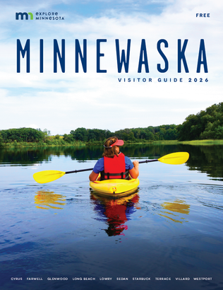 A person and a dog on a paddleboard on a lake at sunset, featured on the cover of the 2024 Minnewaska Visitor Guide.