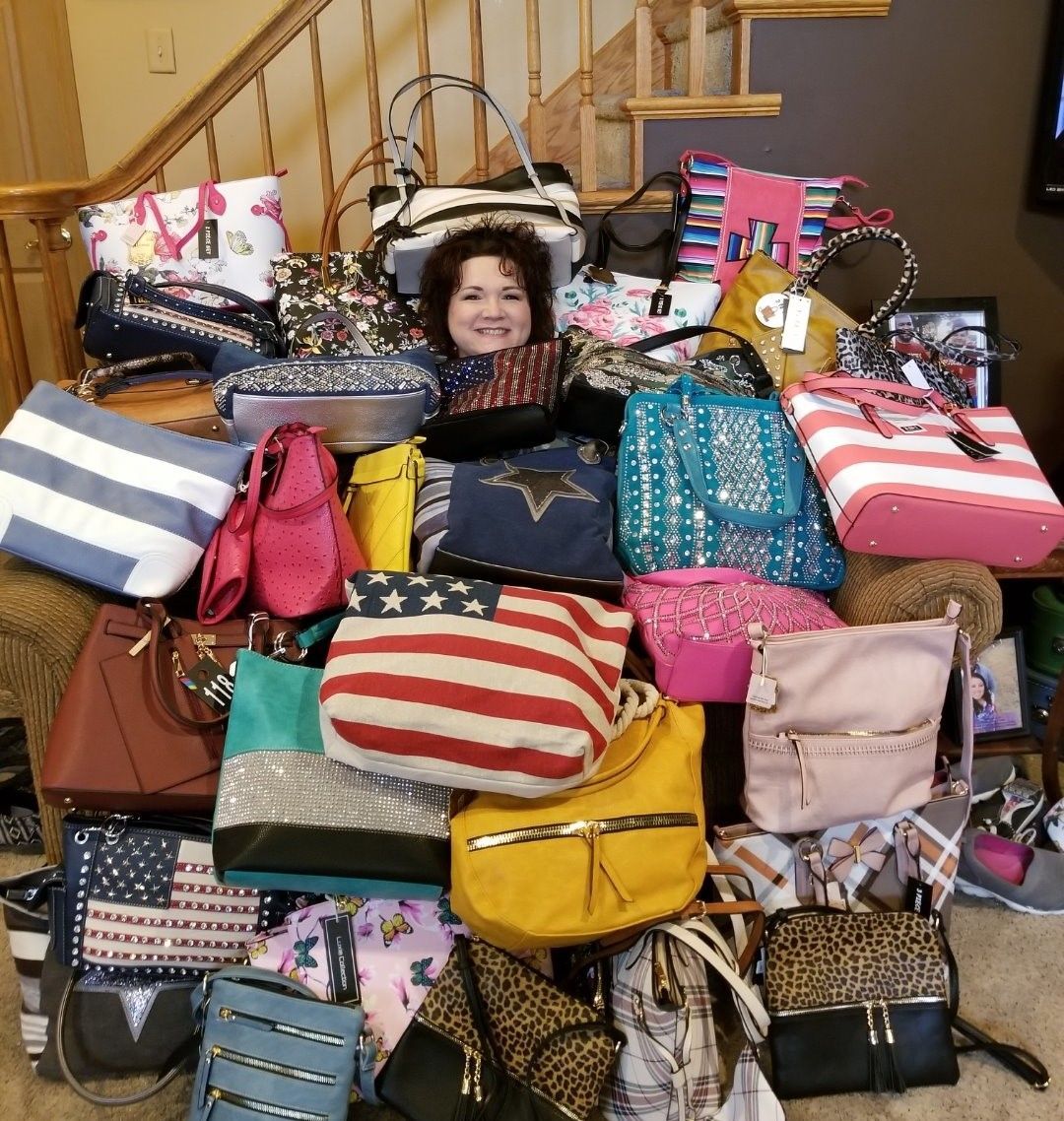 A smiling person peeking out from behind a large pile of colorful, assorted handbags on stairs in a home setting.
