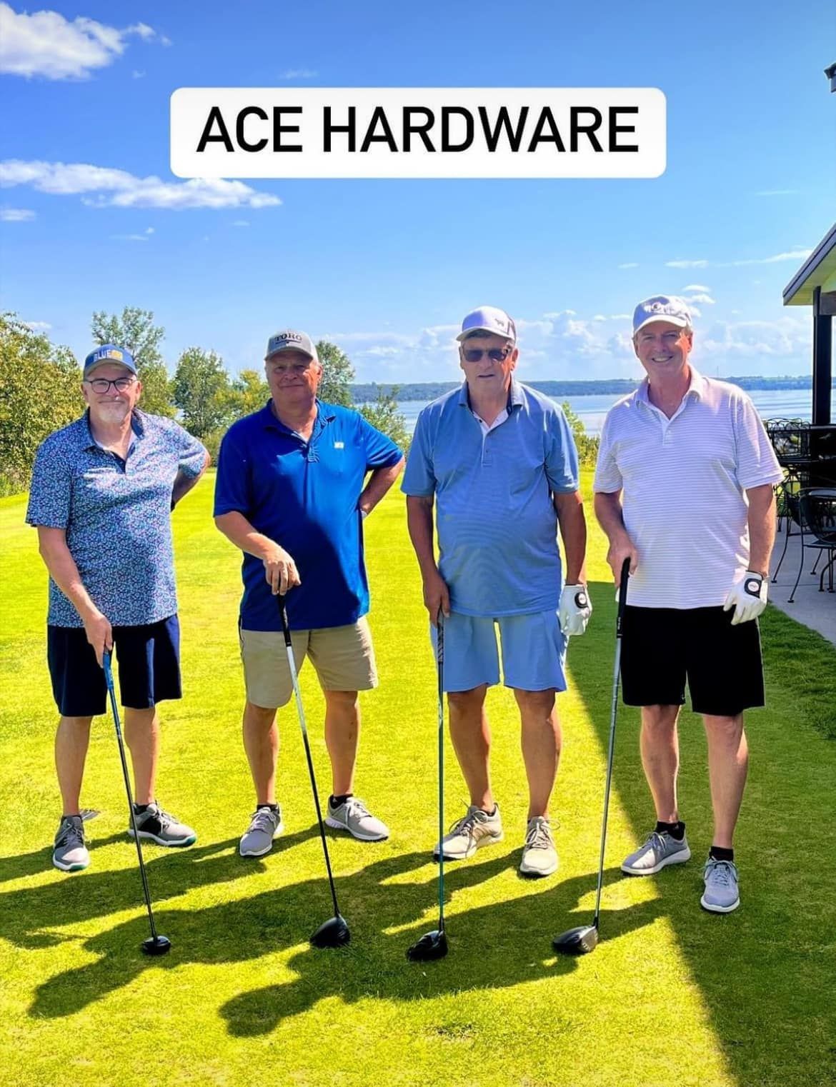 Four people in golf attire standing on a sunny golf course, each holding a golf club, with 