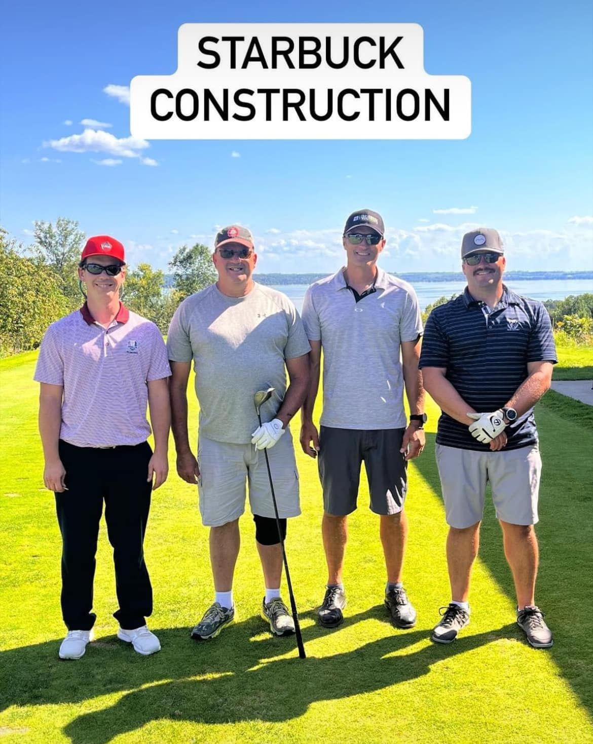 Four people stand together on a grassy golf course under a clear blue sky, with 