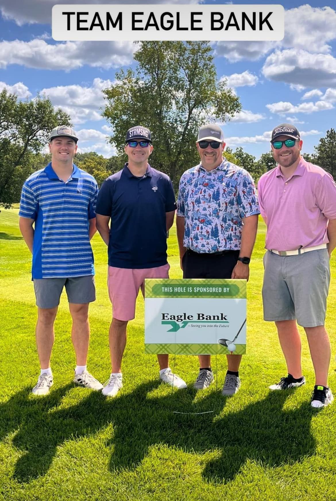 Four people stand on a sunny golf course holding a 