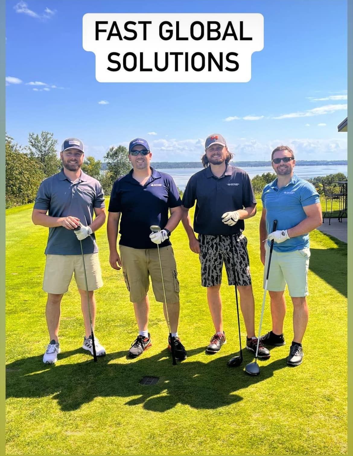 Four people in golf attire standing on a sunny golf course under a sign labeled 