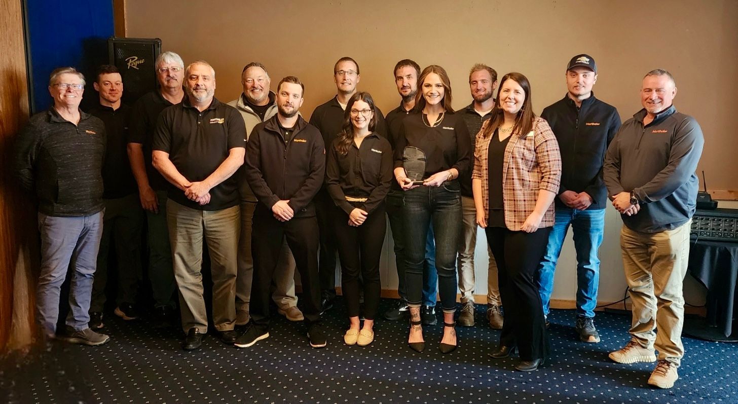 A group of people in business casual attire posing together indoors, with one individual holding an award plaque.
