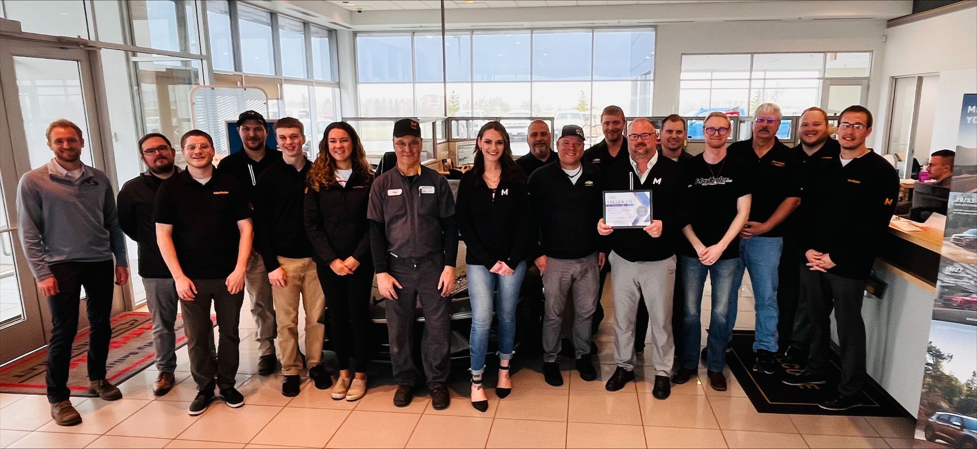 A group of people in a dealership lobby, some holding a certificate, posing for a photo.