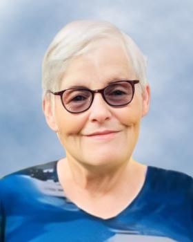 Une femme portant des lunettes et une chemise bleue sourit à la caméra.