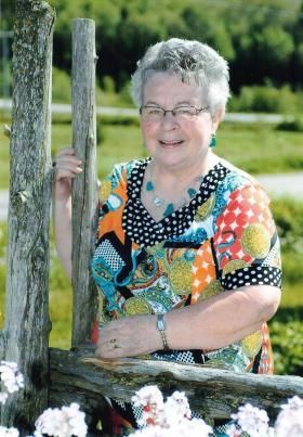 Une femme se tient à côté d'une clôture en bois avec des fleurs en arrière-plan.