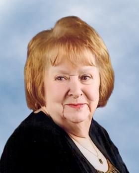 Une femme aux cheveux roux porte un pull noir et un collier.
