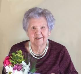 Une femme âgée aux cheveux violets tient un bouquet de fleurs.