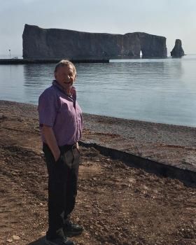 Un homme vêtu d'une chemise violette se tient sur une plage à côté d'un plan d'eau.