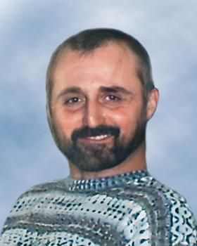 Un homme avec une barbe porte un pull et sourit.