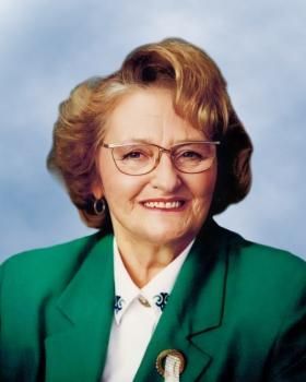 Une femme portant des lunettes et une veste verte sourit.