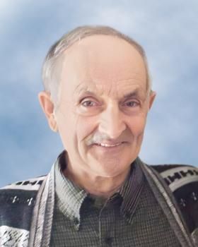 Un homme avec une moustache et un pull sourit à la caméra.