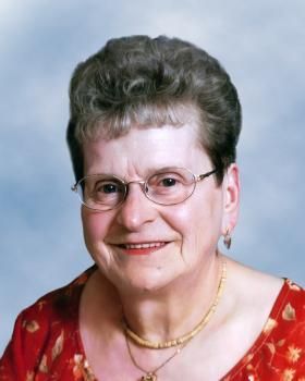 Une femme portant des lunettes et une chemise rouge sourit à la caméra.