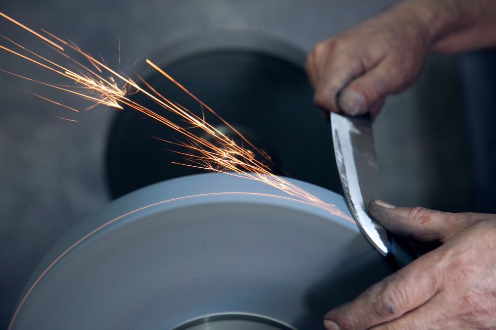 Knife Sharpener and Hand With Blade on Table — Mobile Scissor Sharpening in Gympie, QLD