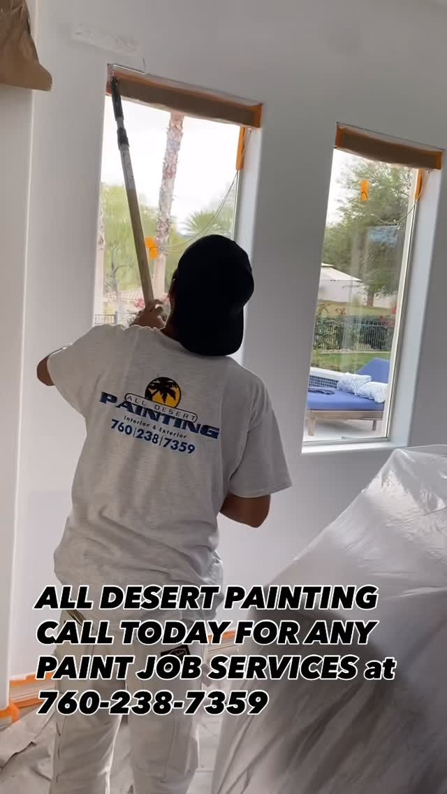 Painter in white shirt masking a window frame in a bright room during interior painting.