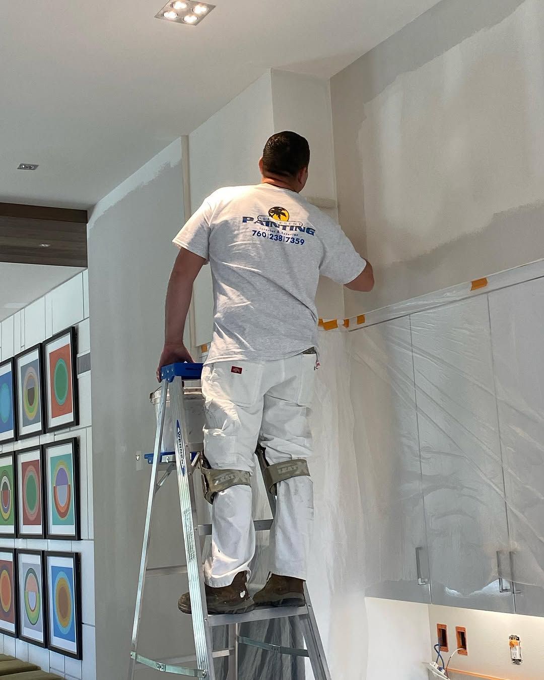 Worker standing on a ladder painting a wall in a bright room