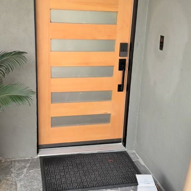 Modern orange front door with horizontal frosted glass panels and a black doormat at the entry.