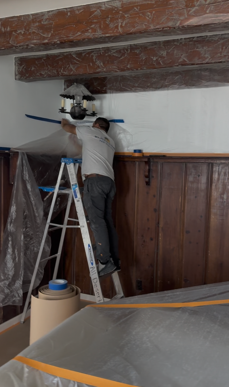 Worker painting interior wall near windows, with “All Desert Painting” contact text at bottom.