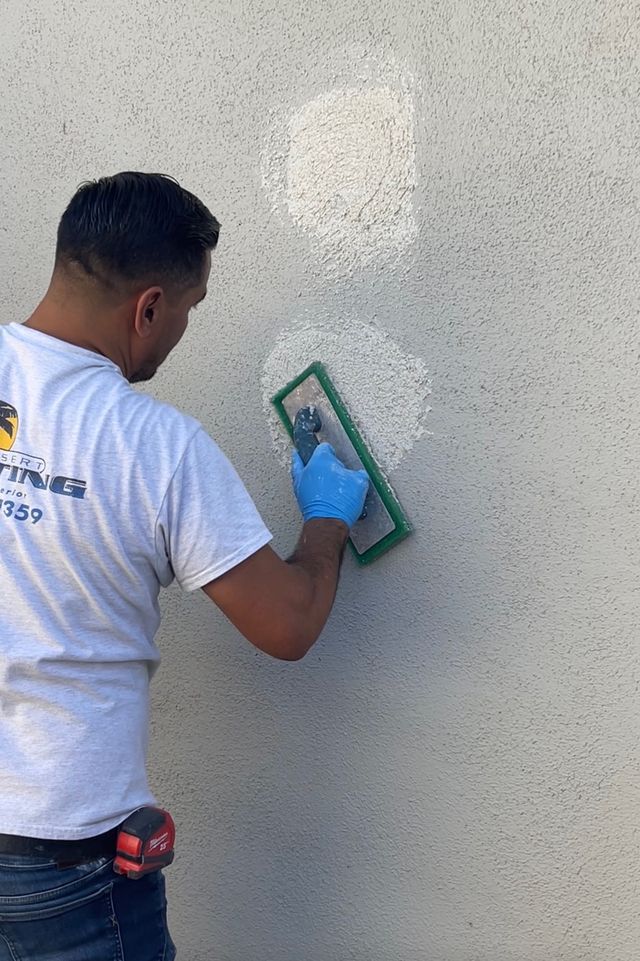 Person painting a wall dark gray with a roller, with white edges and masking tape at the bottom