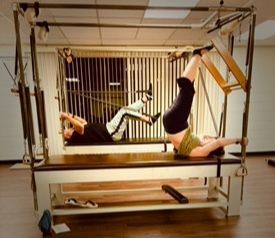 Two adults on Gratz Cadillac equipment performing classical Pilates exercises in Poway, California.  Cadillac Group Class.
