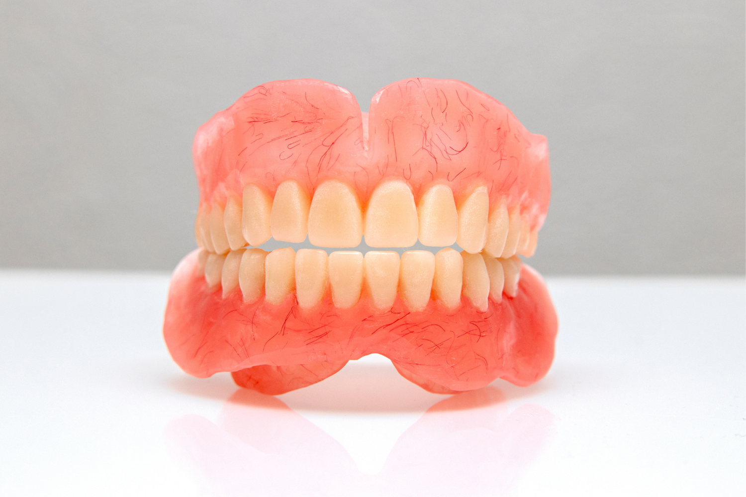 Pink dentures on a white background, showing upper and lower teeth.
