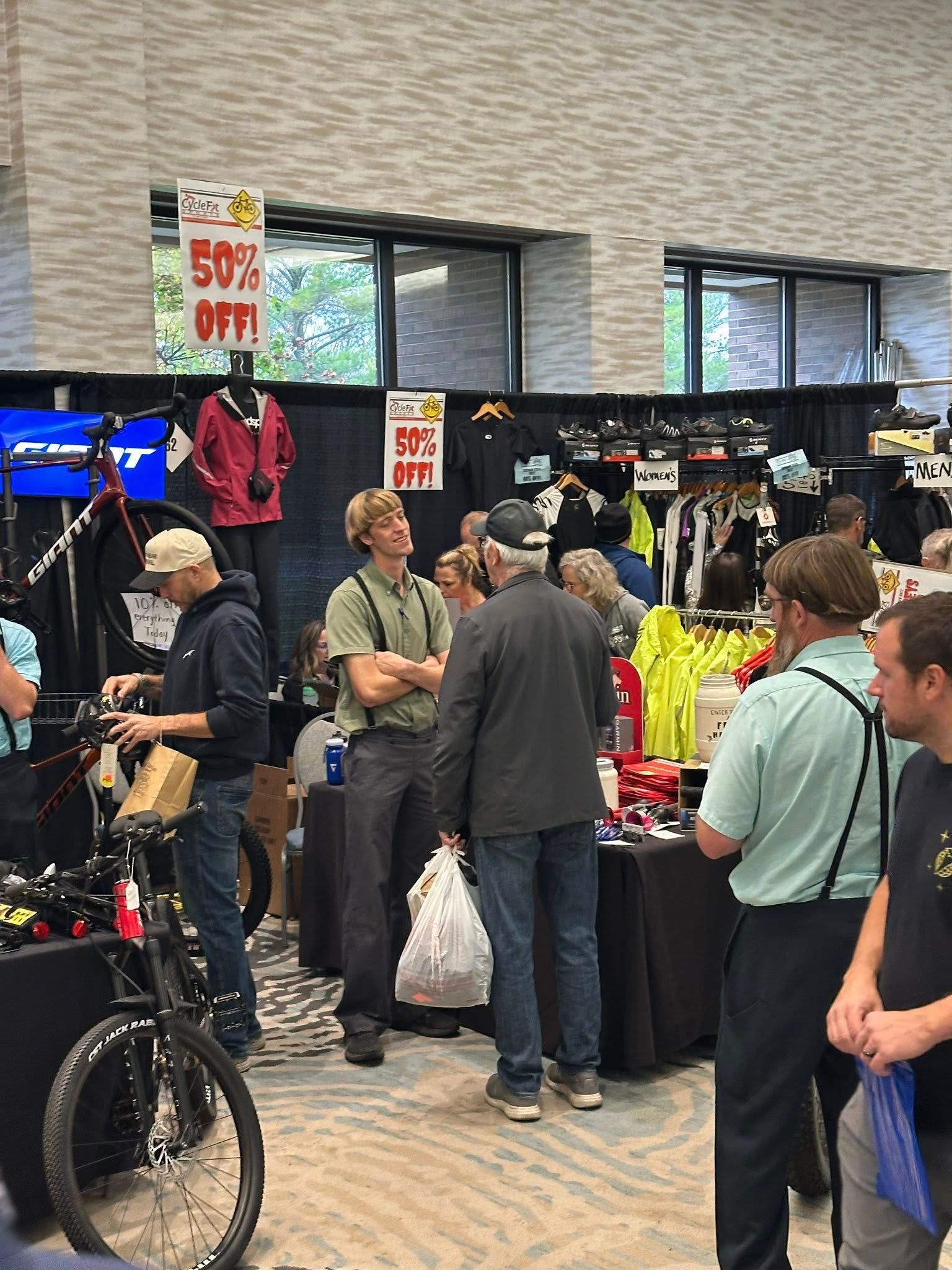A group of people browse sports gear and bicycles at an indoor trade show with