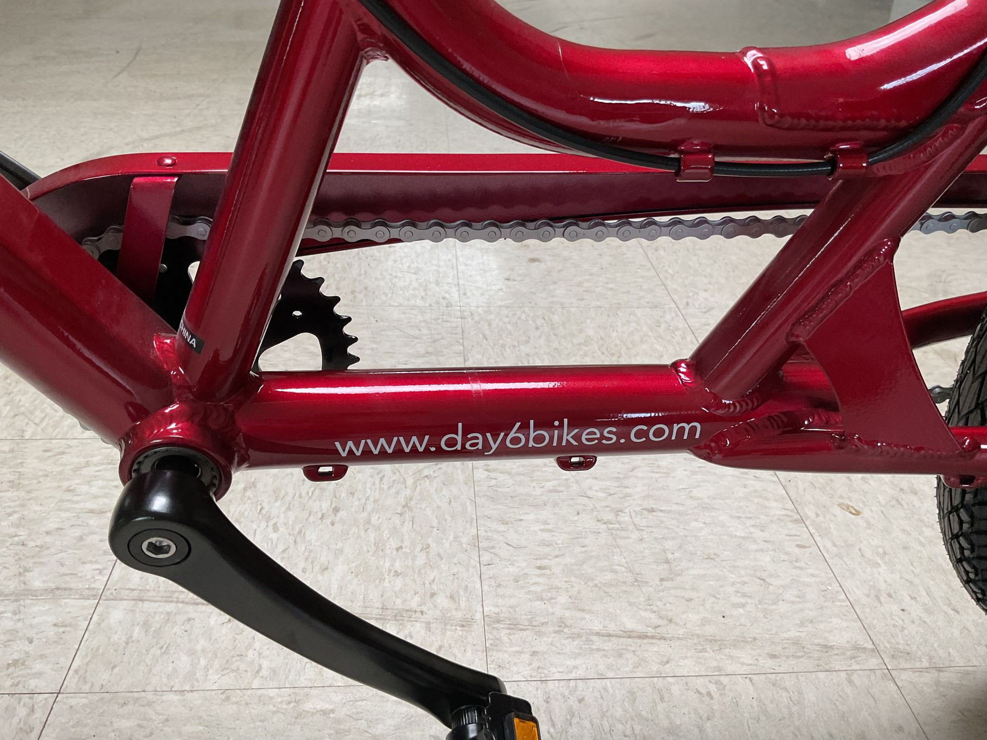 The central frame of a red bicycle, featuring the web address www.day6bikes.com printed on the lower horizontal tube.