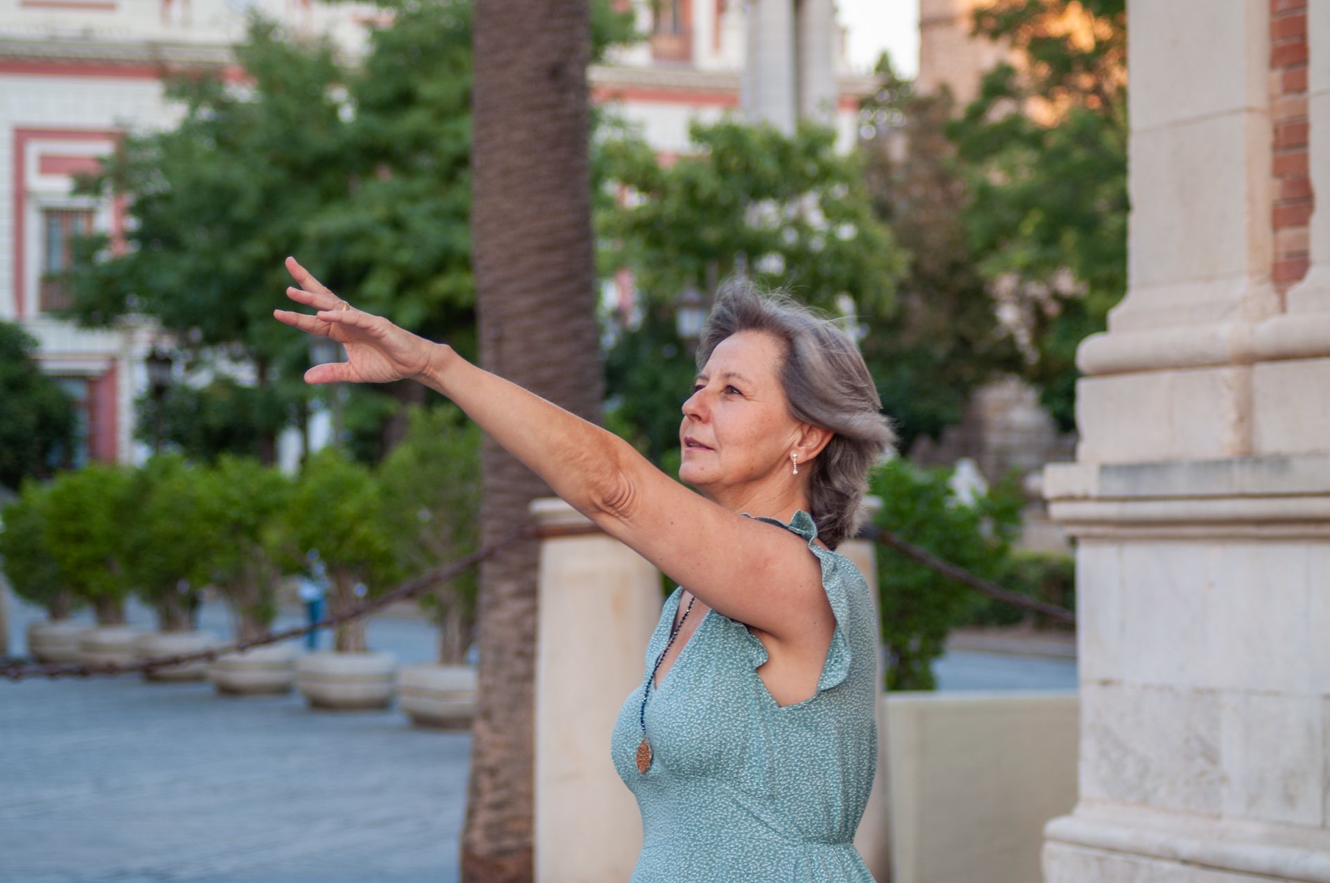 An older woman is standing in front of a building with her arms outstretched.