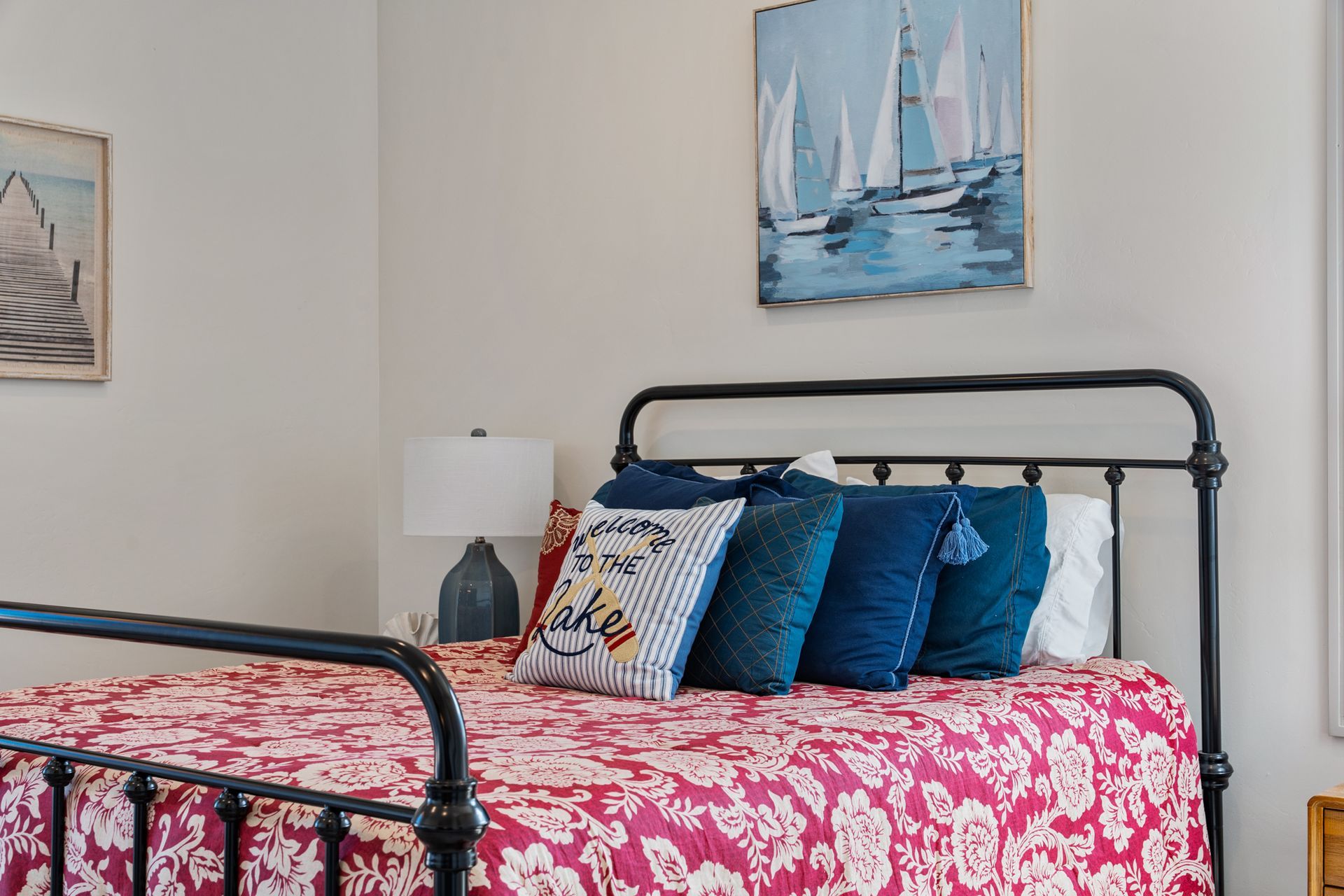 Bedroom with black metal bed, pink floral quilt, blue pillows, and sailboat wall art