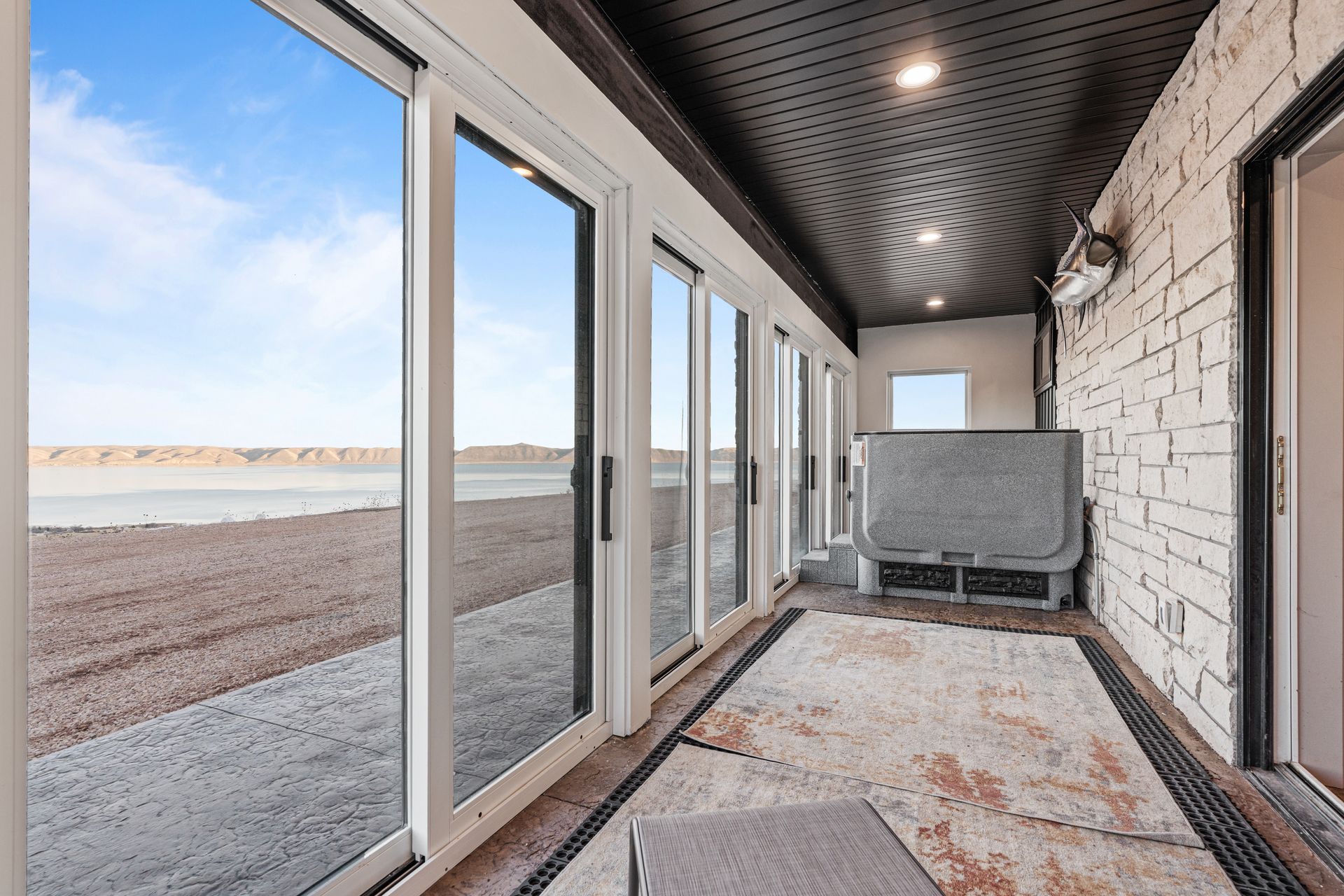 Enclosed porch with large windows, patterned rug, and a lake view beyond the open door.