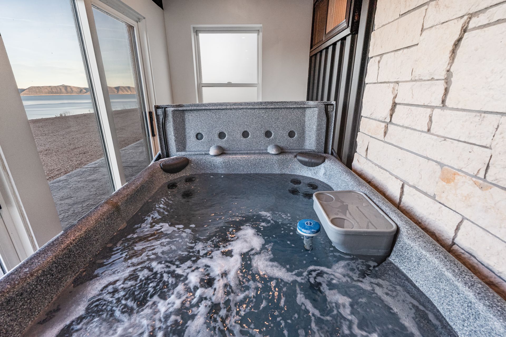 Indoor hot tub with bubbling water, gray stone walls, and a windowed spa room