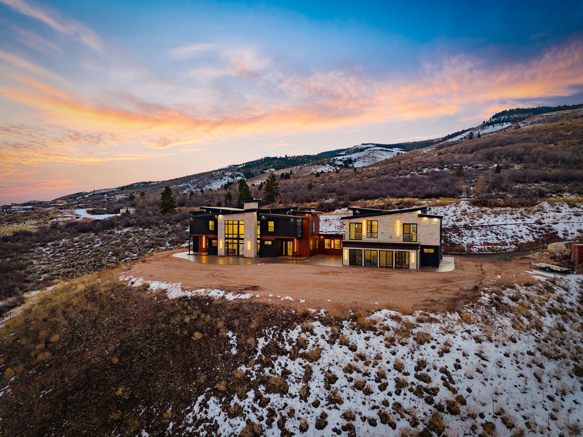Modern house lit at sunset on a snowy hillside under a colorful sky