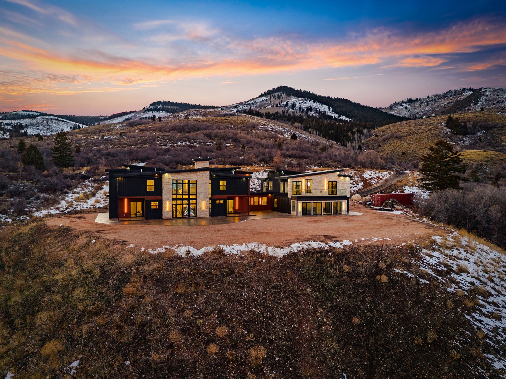 Modern house on a snowy hill at sunset, with mountains and a pastel sky in the background.