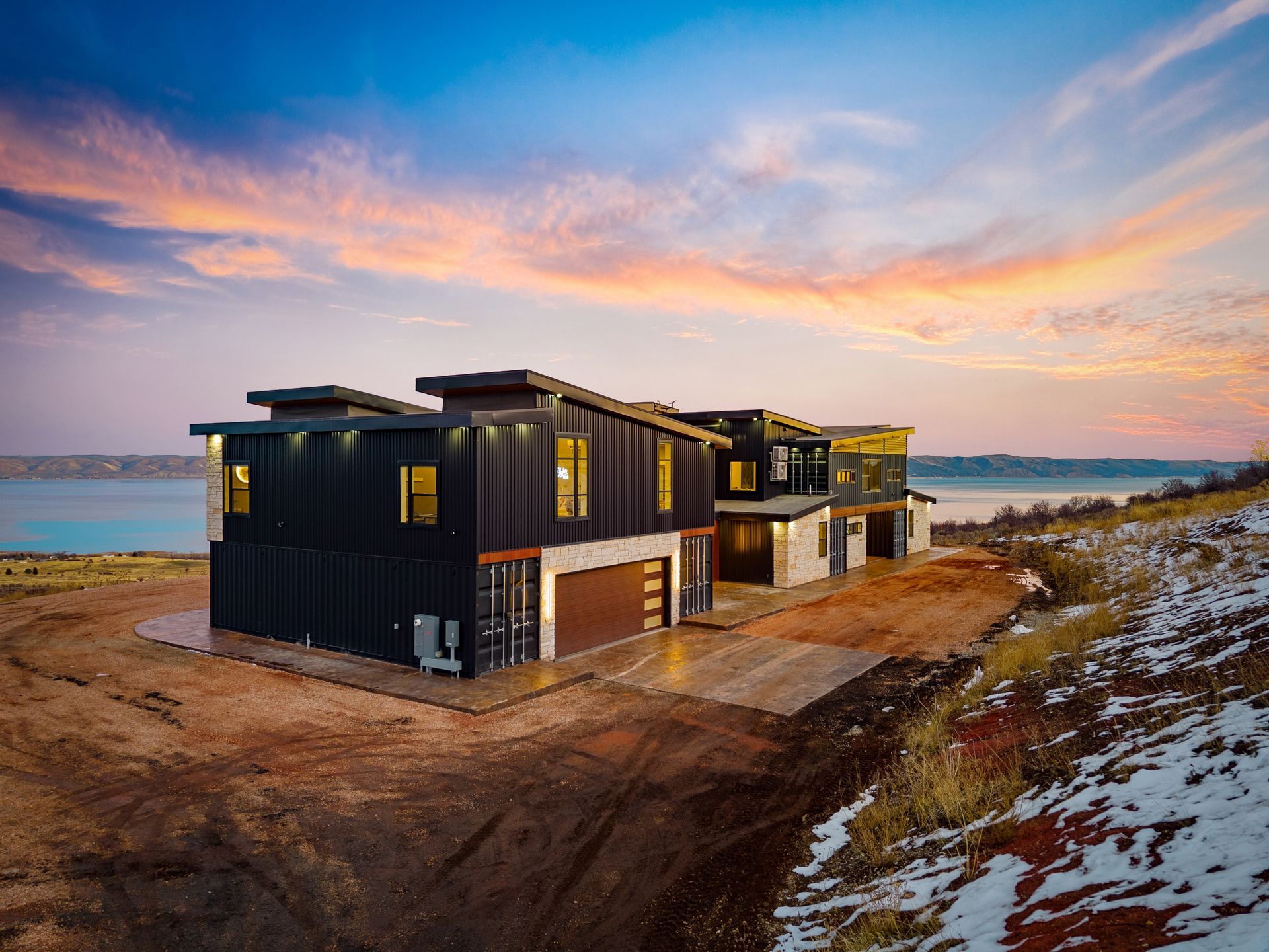 Modern black house by the sea at sunset, with snowy ground and a colorful sky