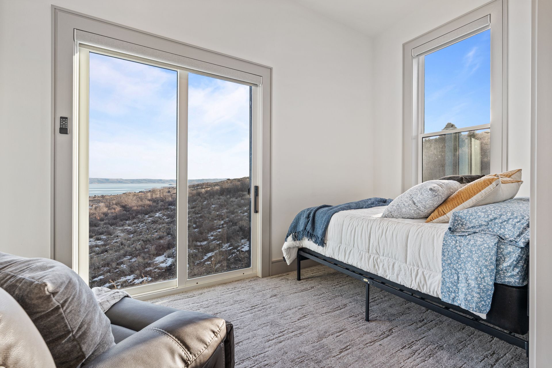 Bright bedroom with bed, chair, and large windows overlooking a rocky shoreline