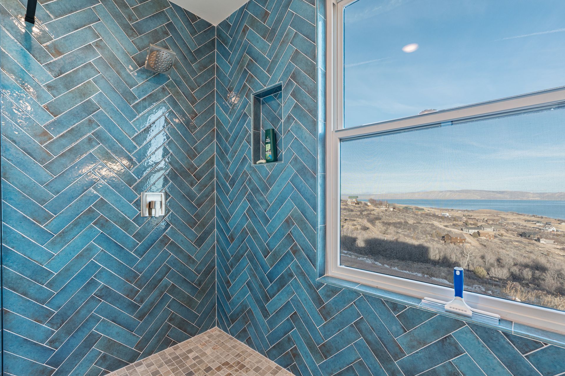 Blue-tiled shower corner with window overlooking a beach and ocean.