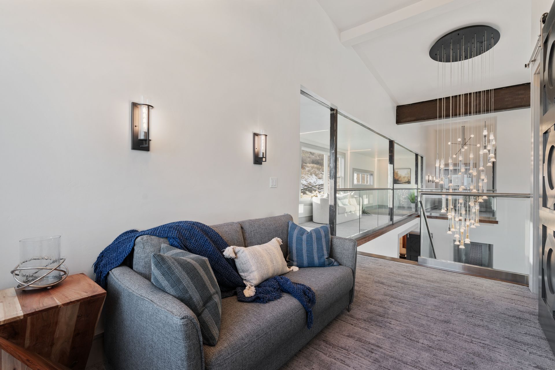 Modern living room with gray sofa, blue throw pillows, and glass wall overlooking a bright interior.