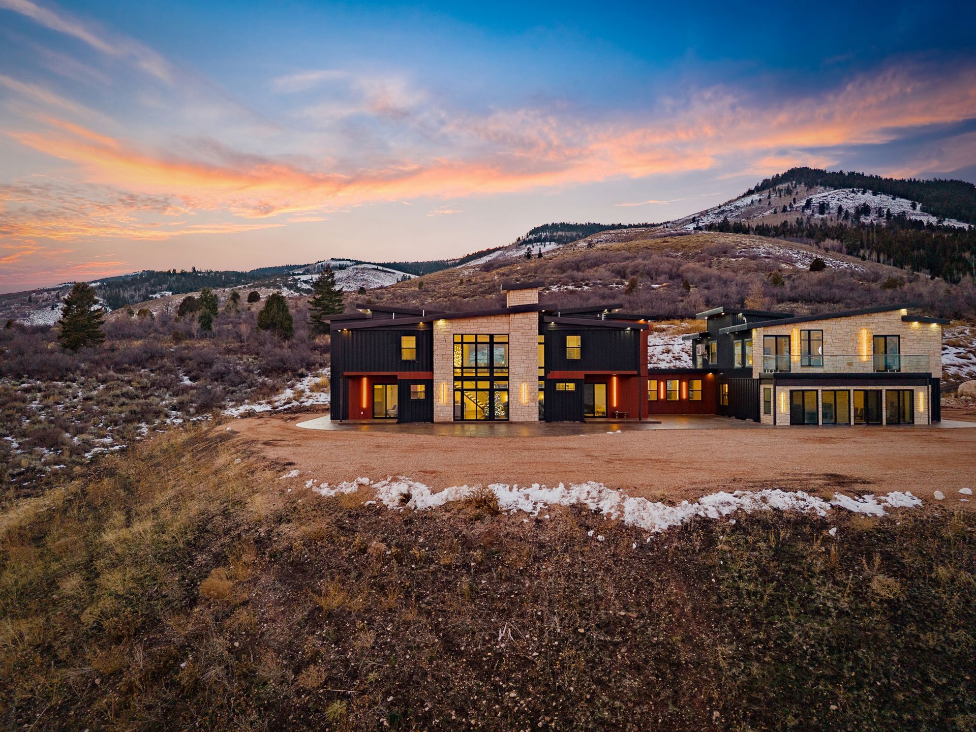 Modern house with warm lights in a snowy hillside landscape at sunset
