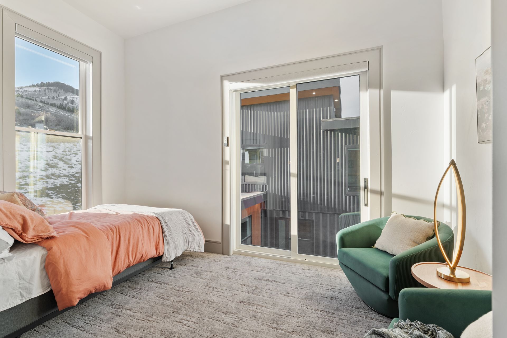 Bright bedroom with bed, green chair, and sliding glass doors to a balcony