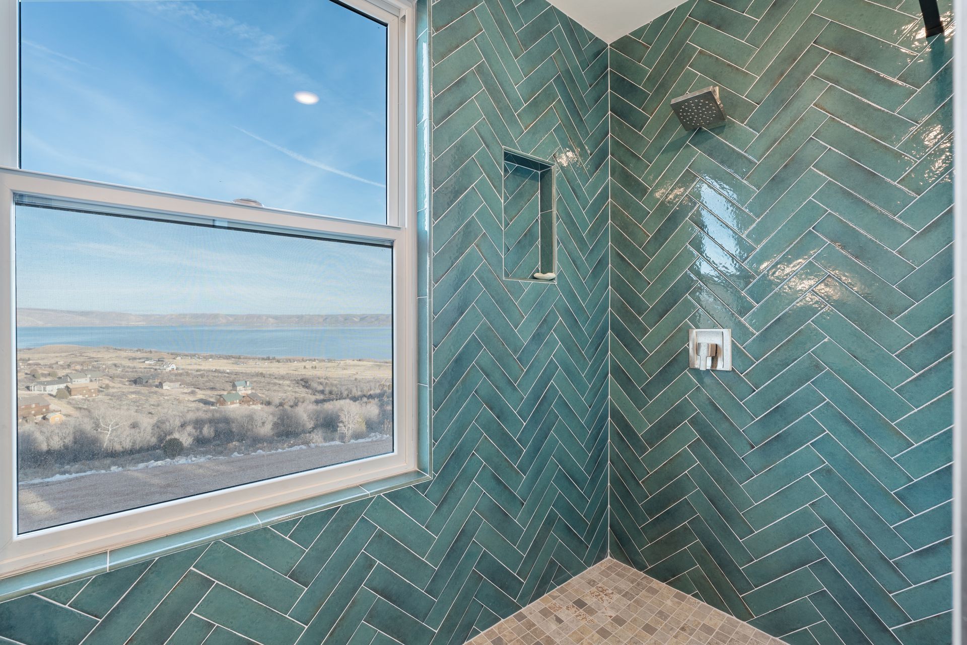 Bathroom shower with teal herringbone tile and a window overlooking the water