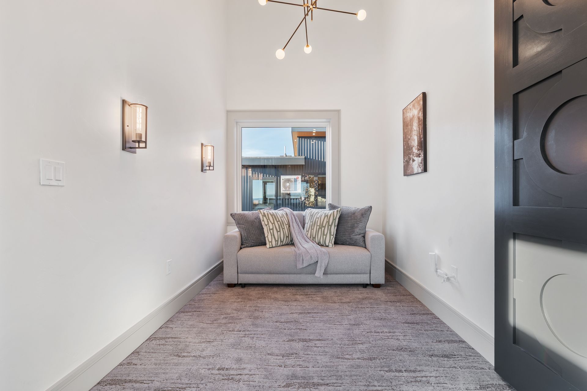 Bright hallway with a gray sofa at the end, wall sconces, and a black front door.