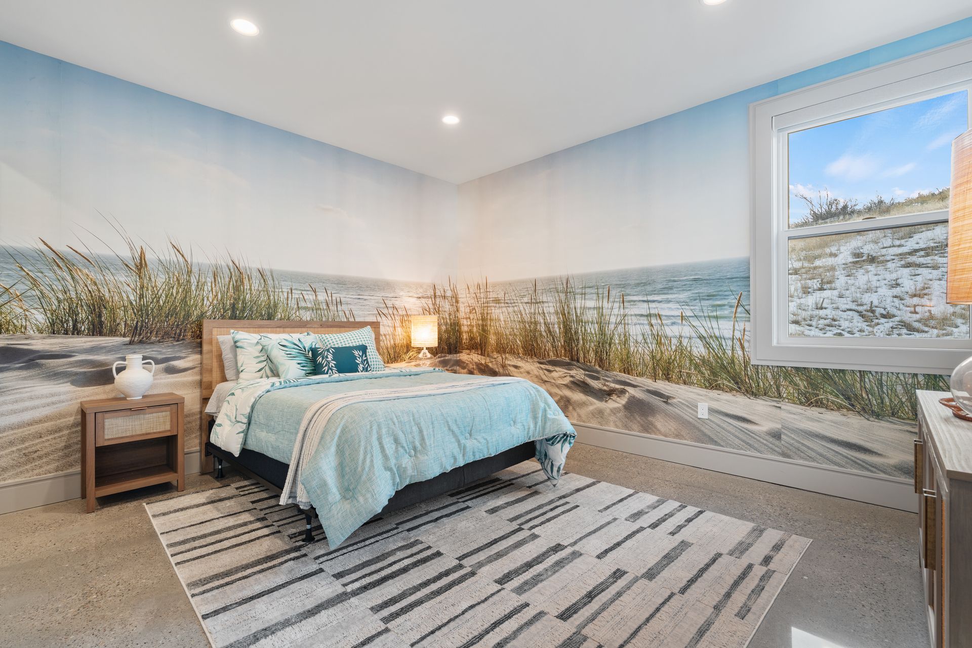 Beach-themed bedroom with ocean mural, teal bedding, striped rug, and a large window.