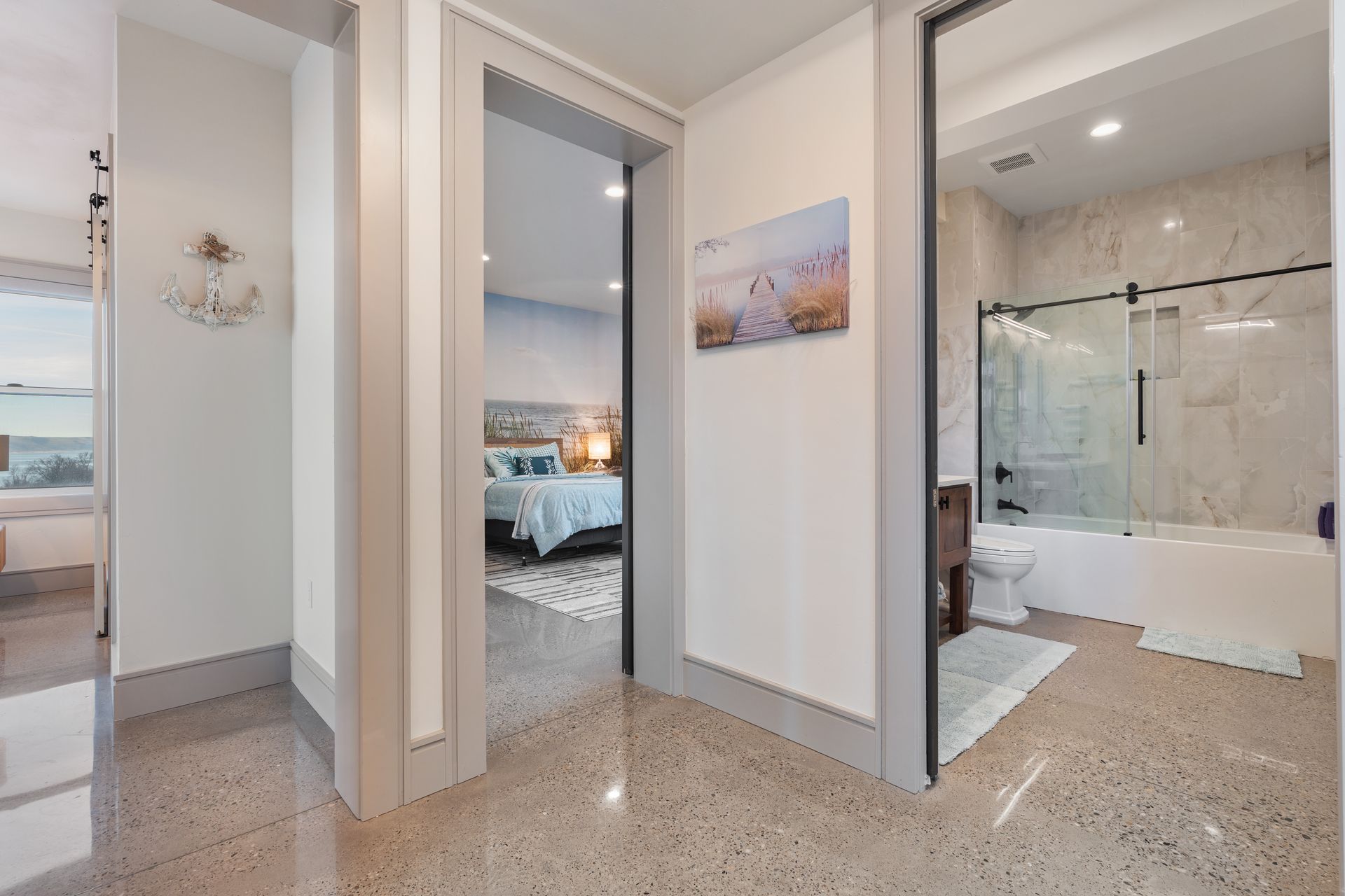 Bright modern hallway leading to a bedroom and tiled bathroom with a glass shower and freestanding tub
