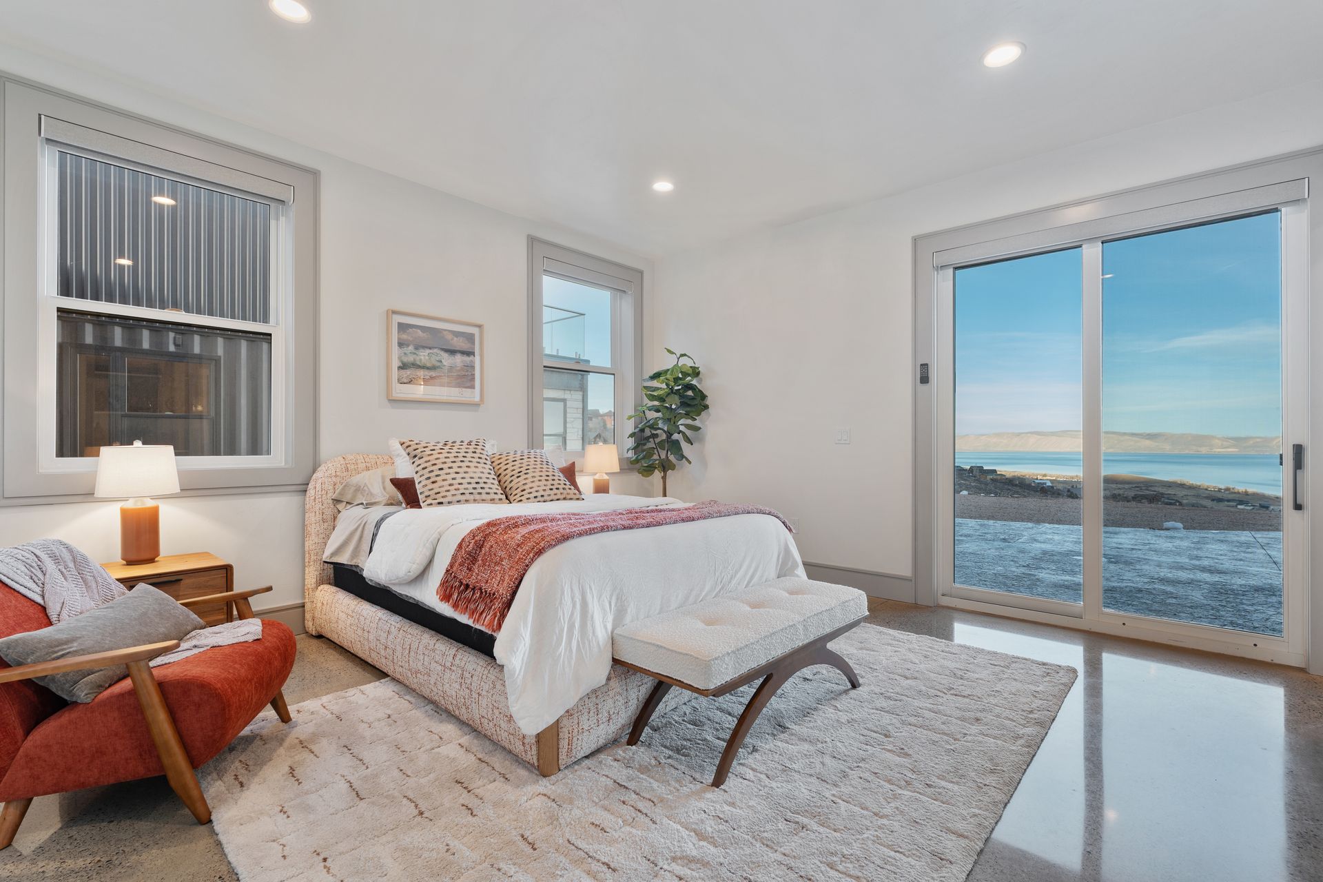 Bright bedroom with a bed, orange chair, and large sliding doors overlooking the ocean