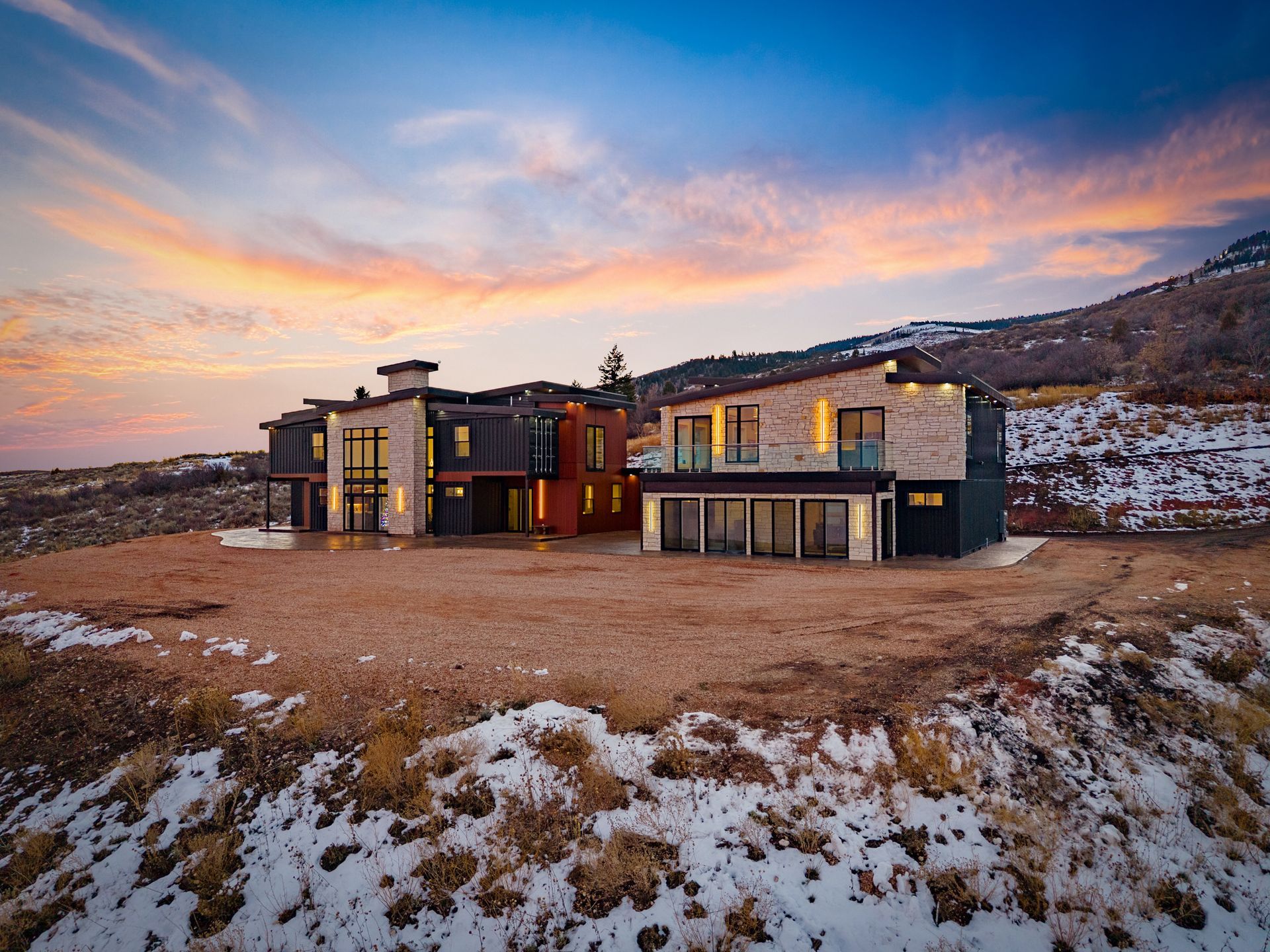 Modern house at sunset in a snowy, rocky landscape with large windows and warm interior lights