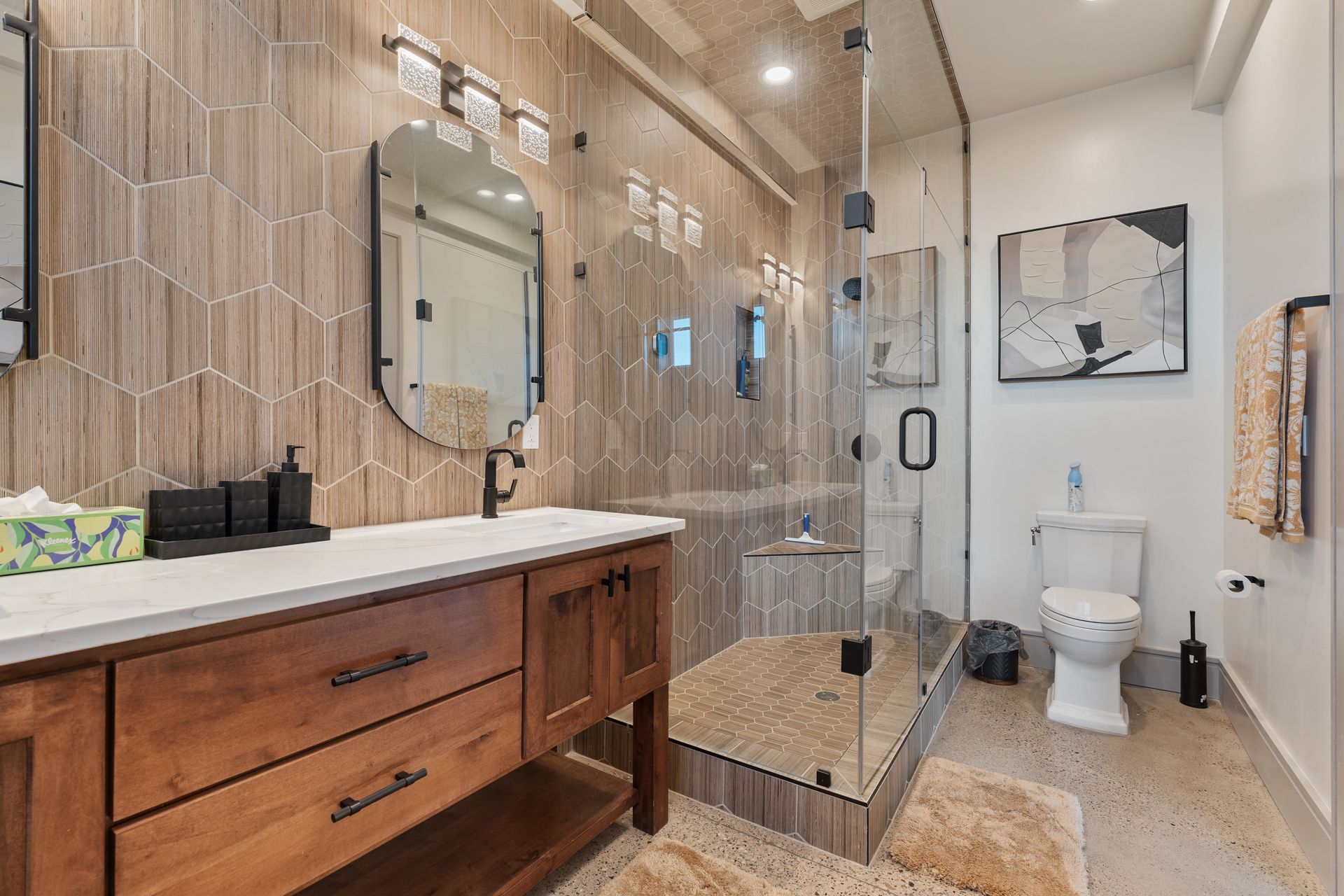 Modern bathroom with double vanity, glass shower, white toilet, and tan tile walls