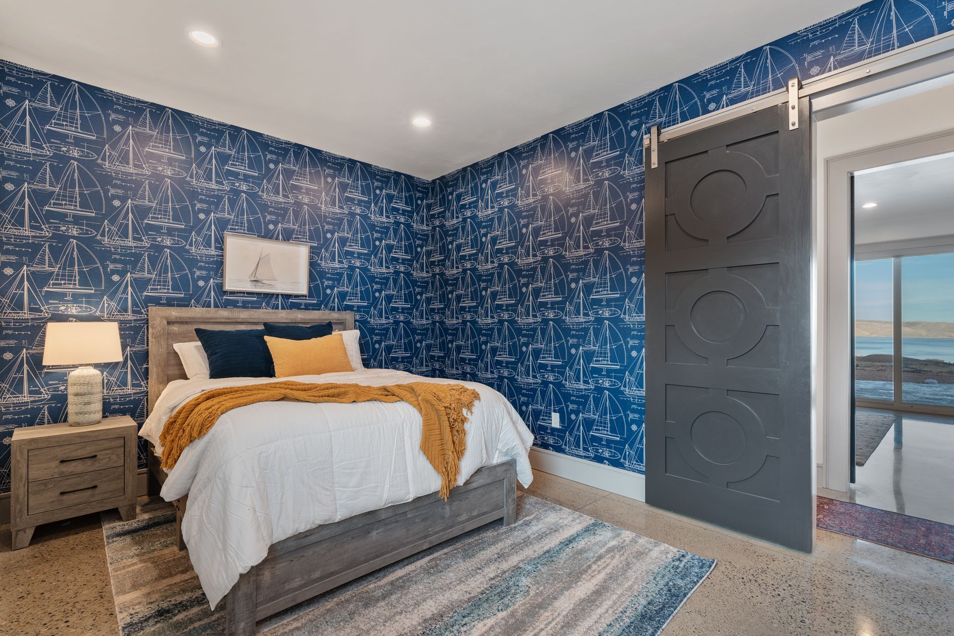 Cozy bedroom with blue patterned walls, a bed, nightstand, and open door to a balcony view.