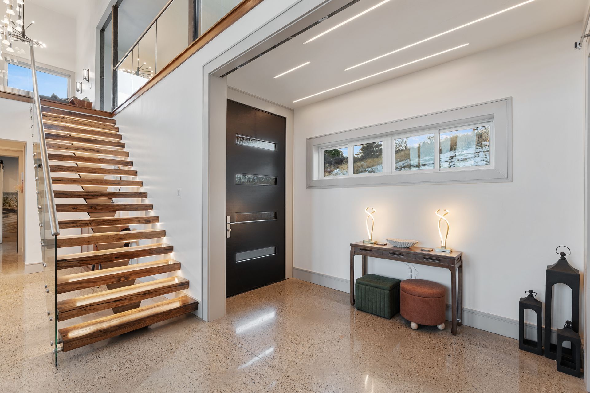 Modern entryway with wooden staircase, black door, console table, and floor lanterns