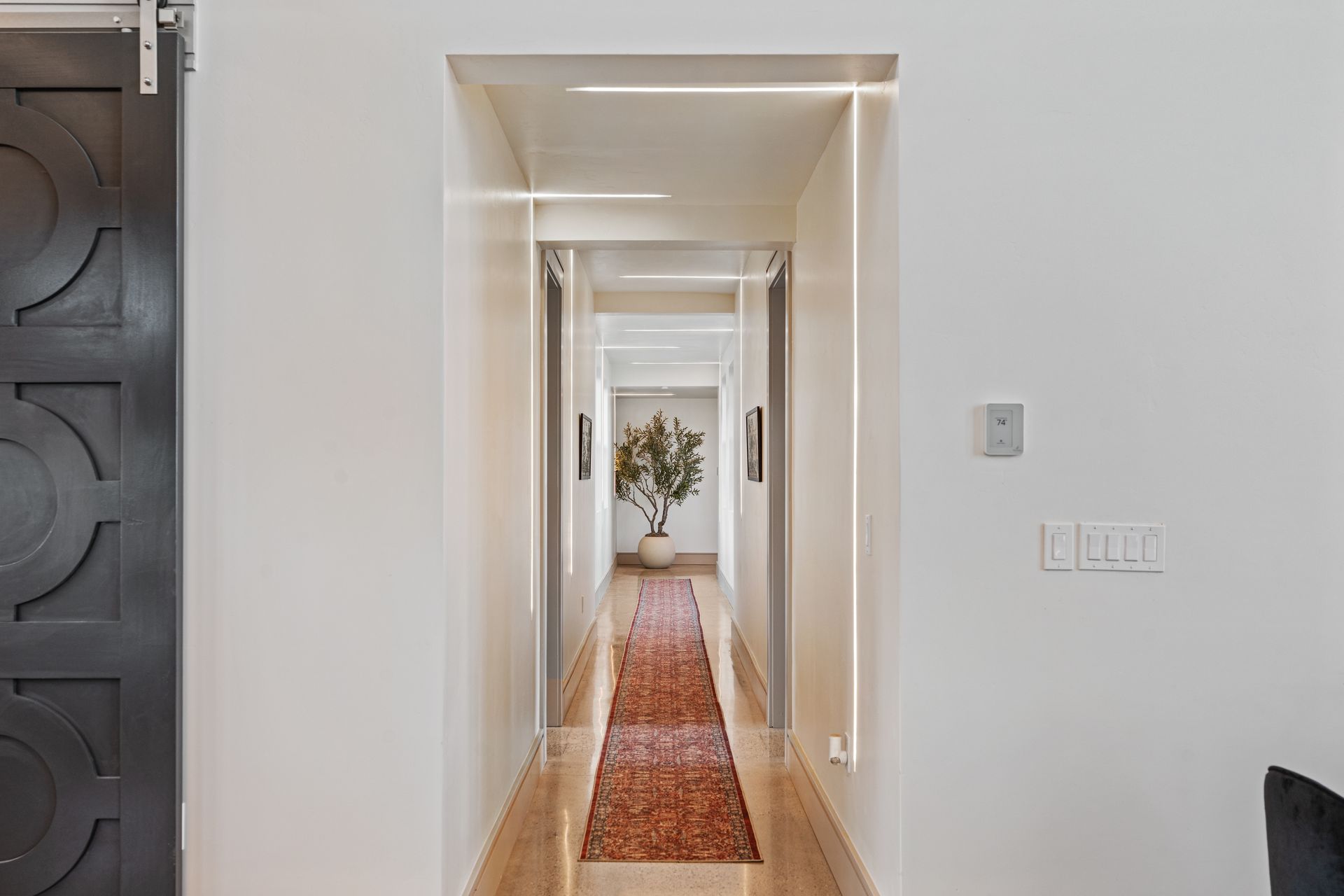 Bright hallway with white walls, a red runner rug, and a vase of flowers at the far end.